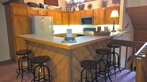 A kitchen with wooden cabinets, a refrigerator, a microwave, and a bar area with stools. - Snowcreek Resort Vacation Rental 456 (Mammoth Lakes)