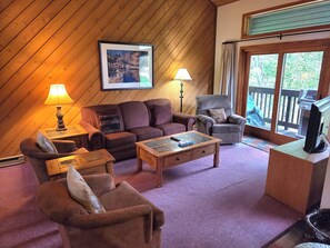 A cozy living room with a wooden ceiling, a sofa, armchairs, a coffee table, and a television. - Snowcreek Resort Vacation Rental 456 (Mammoth Lakes)
