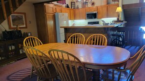 A dining area with a wooden table and chairs, a kitchen with wooden cabinets, and a microwave above the counter.