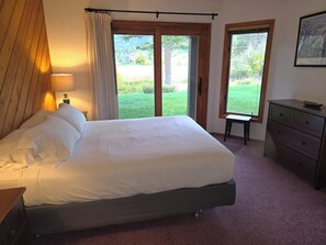 A bedroom with a bed, a nightstand, a dresser, and a window with a view of a lawn. - Snowcreek Resort Vacation Rental 456 (Mammoth Lakes)