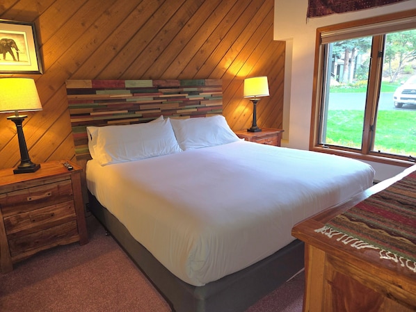 Un lit bien fait dans une pièce dont le plafond et les murs sont recouverts de lambris en bois, une fenêtre donnant sur l’extérieur et deux tables de chevet avec des lampes.