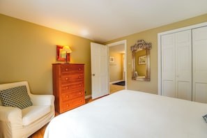 Un dormitorio con cama, cómoda, silla y puerta que da a otra habitación.