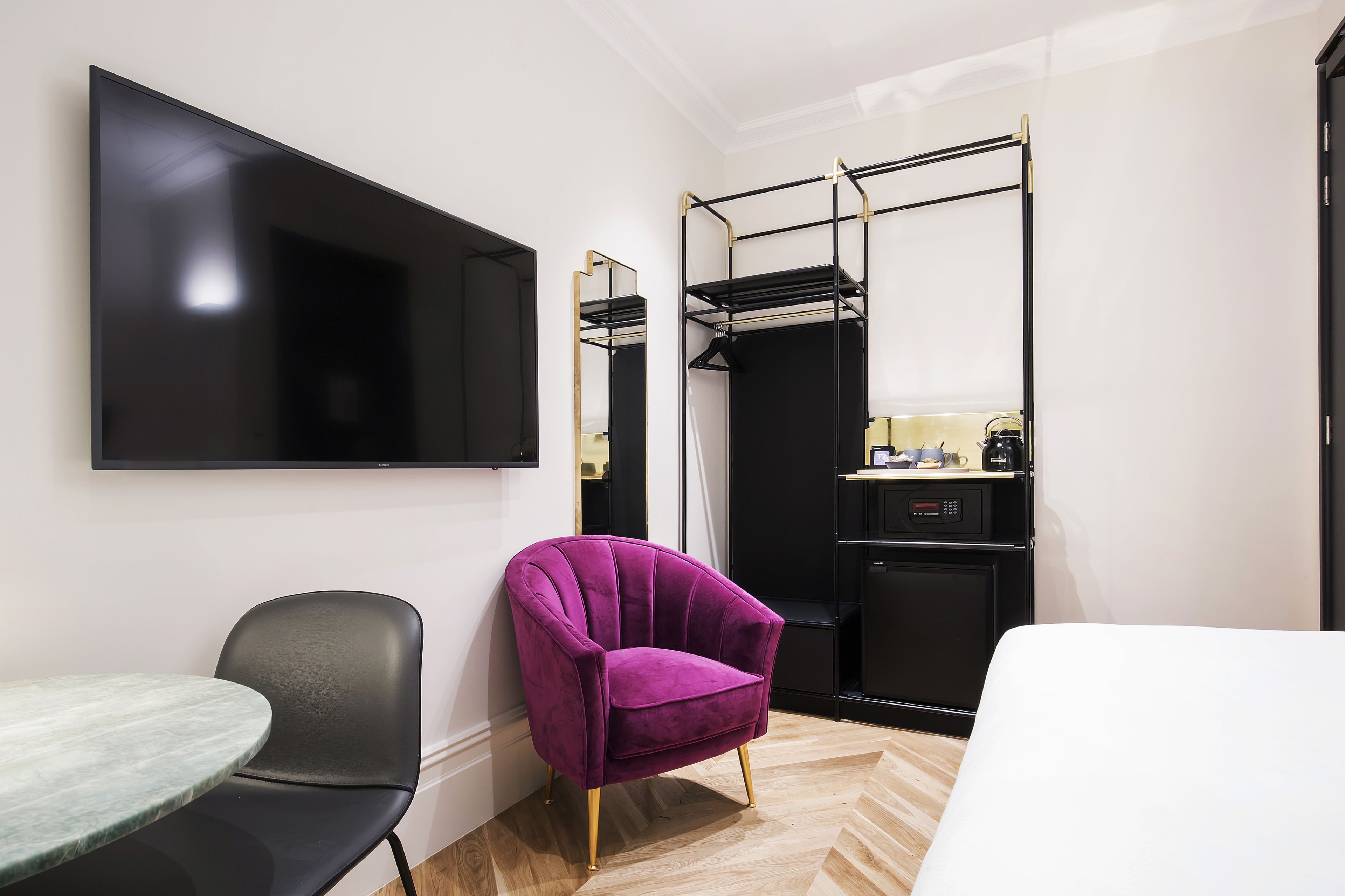 Ein modernes Hotelzimmer mit Flachbildfernseher, einem violetten Sessel, einem kleinen Tisch und einer kompakten Küchenzeile.