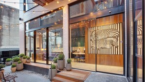 Un bâtiment moderne doté de grandes portes vitrées, d’une porte en bois ornée de motifs zébrés, d’un espace extérieur aménagé pour s’asseoir et de plantes en pot.