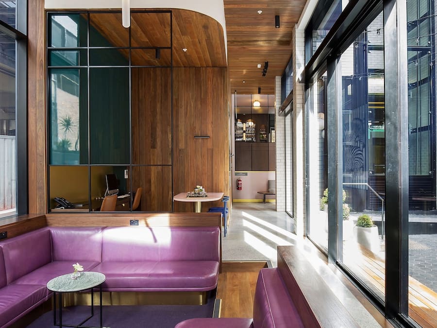 Een modern interieur met houten plafond, paarse zitplaatsen en grote ramen.