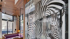 Un intérieur moderne agrémenté d’une grande fresque représentant des zèbres, de lambris en bois, d’un canapé violet et d’un coin repas avec des chaises bleues.