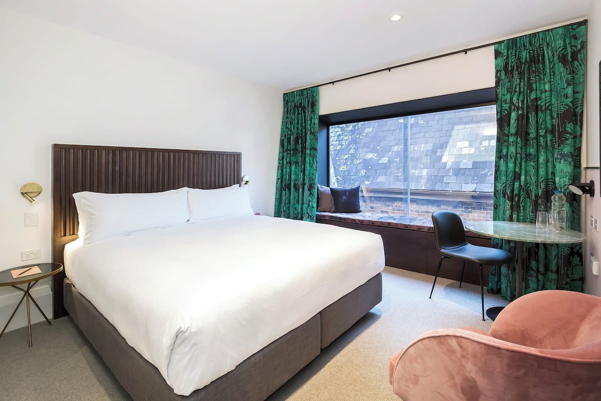 Habitación de hotel moderna con una cama grande, una mesita redonda pequeña, una silla y vistas al exterior.