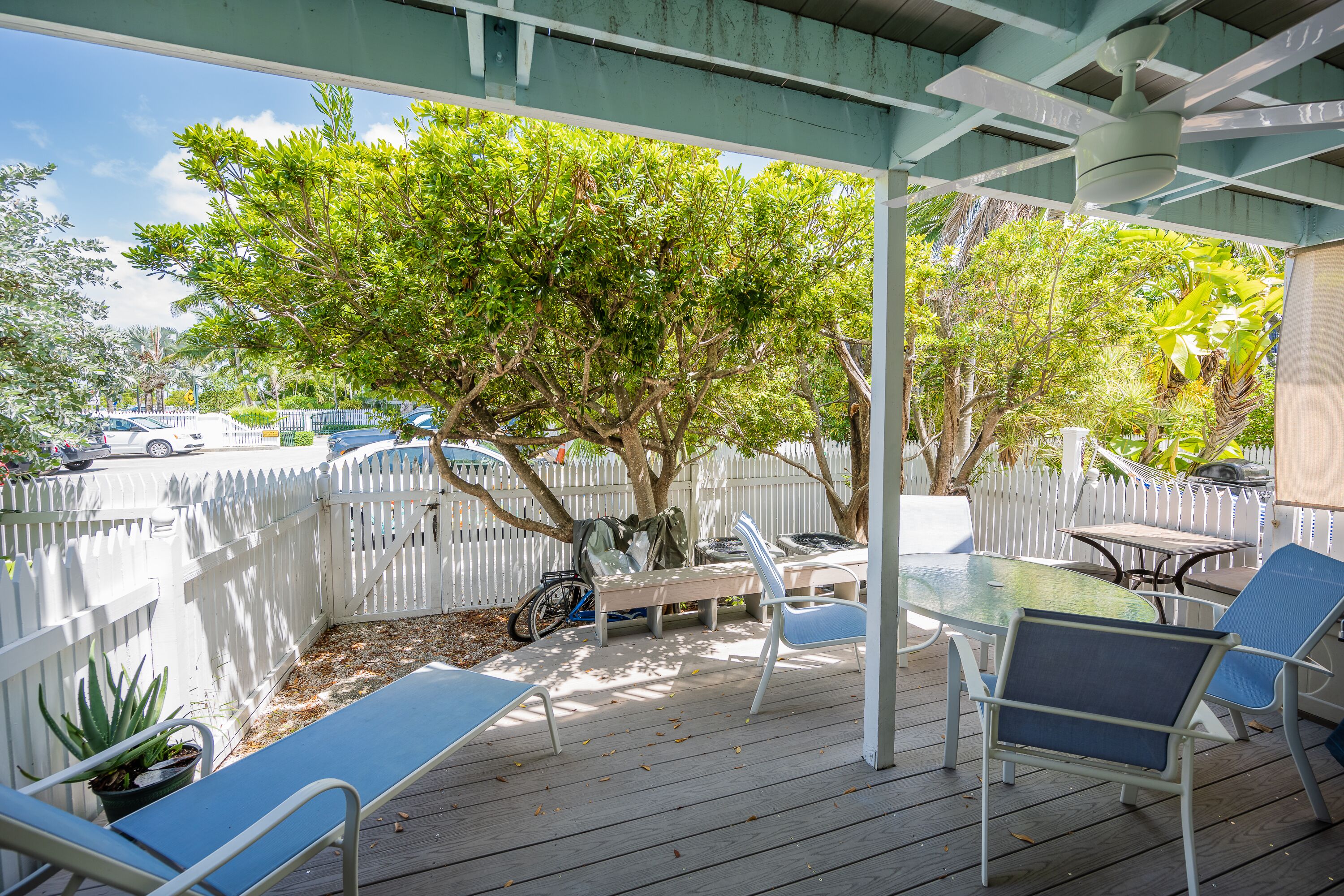 A covered outdoor patio with a white fence, a table, chairs, and a bicycle.