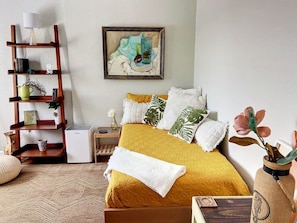 Ein ordentlich eingerichtetes Schlafzimmer mit Bett, Nachttisch, Lampe und einem an der Wand befestigten Regal mit verschiedenen Gegenständen.