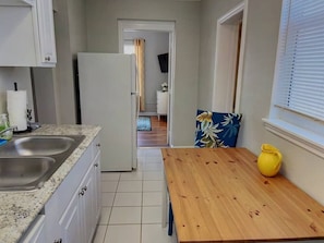 A kitchen with a wooden table, a yellow pitcher, and a view into the adjacent room. - Boho Charm, Historic 1br -Steps to downtown (Melbourne)