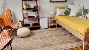 A bedroom with a bed, a chair, a bookshelf, a small table, and a wall clock. - Boho Charm, Historic 1br -Steps to downtown (Melbourne)