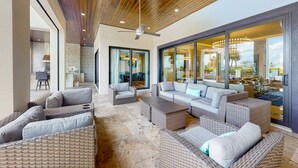 Un vaste espace de vie extérieur aménagé avec des meubles en osier, un ventilateur de plafond et de grandes portes vitrées donnant sur un patio.