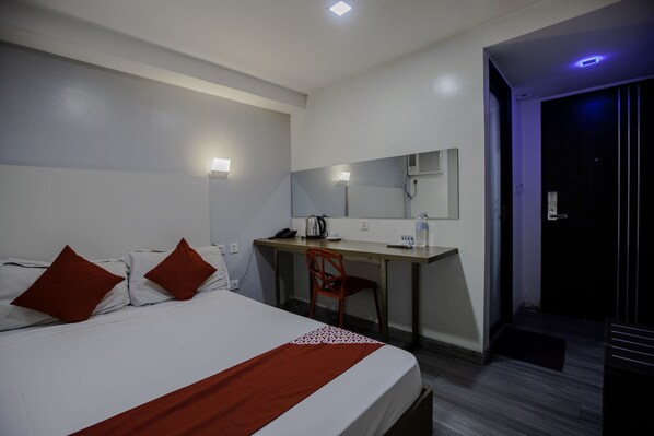 A hotel room with a bed, a desk, a chair, a mirror, and a door. - Mc Hotel Fairview (Quezon City)