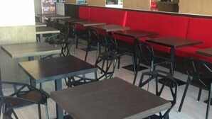 Interior de restaurante con varias mesas y sillas, detalles en rojo en las paredes y decoraciones de papel colgantes.