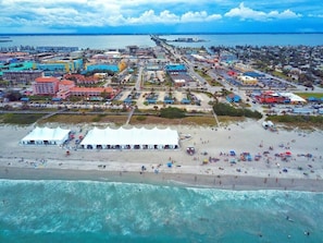 Vue aĂ©rienne dâune ville cĂŽtiĂšre avec une plage, des bĂątiments et une jetĂ©e qui sâavance dans lâeau.