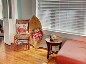 Une piĂšce comprenant une chaise en bois, une planche de surf, une petite table ronde et un lit.