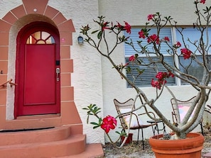 Une porte rouge, un bĂątiment blanc, une plante en pot et une chaise.