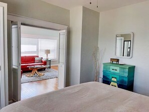 Un dormitorio con cama, cómoda, espejo y un sofá rojo en la zona de estar contigua.