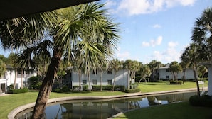 A well-maintained courtyard with a central pond, surrounded by neatly trimmed grass and palm trees. - Bayside 2BR on Whitney Beach w Canal Views, Pool, and Private Lanai  by RVA (Longboat Key)