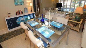 A modern living room with a glass dining table, white sofas, and a flat-screen TV. - Bayside 2BR on Whitney Beach w Canal Views, Pool, and Private Lanai  by RVA (Longboat Key)