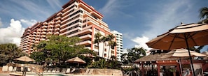 A multi-story hotel with balconies, a pool area with lounge chairs, and umbrellas.
