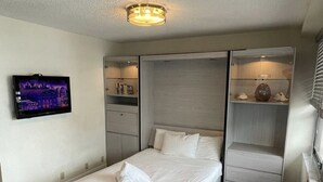 Un dormitorio moderno con cama, estanterías empotradas, televisor de pantalla plana y lámpara en el techo.