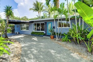Une maison moderne avec une allée pavée, une porte bleue et un jardin agrémenté de différentes plantes.