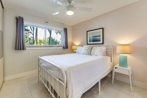 Une chambre à coucher avec un lit, une fenêtre avec des rideaux, un ventilateur de plafond, une lampe de chevet et un tableau encadré accroché au mur.
