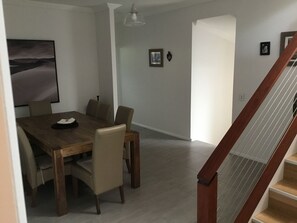 A dining area with a wooden table and chairs, a framed picture on the wall, and a staircase with a wooden railing.