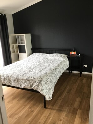 A bedroom with a bed, a nightstand, a wardrobe, and a dark wall.