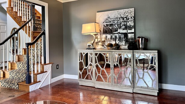 A staircase with a wooden finish and white balusters, a mirrored console table with a geometric design, and a black and white abstract painting on the wall. - WOW ~ Watch the Sun Set from your Private Balcony ~ Family Gatherings  (Topeka)