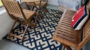 A covered porch with a wooden table and chairs, a patterned rug, and a sofa with a decorative pillow. - Screened porch, Lake Huron views, quiet sub, walk to beach and town in minutes! (Port Austin)