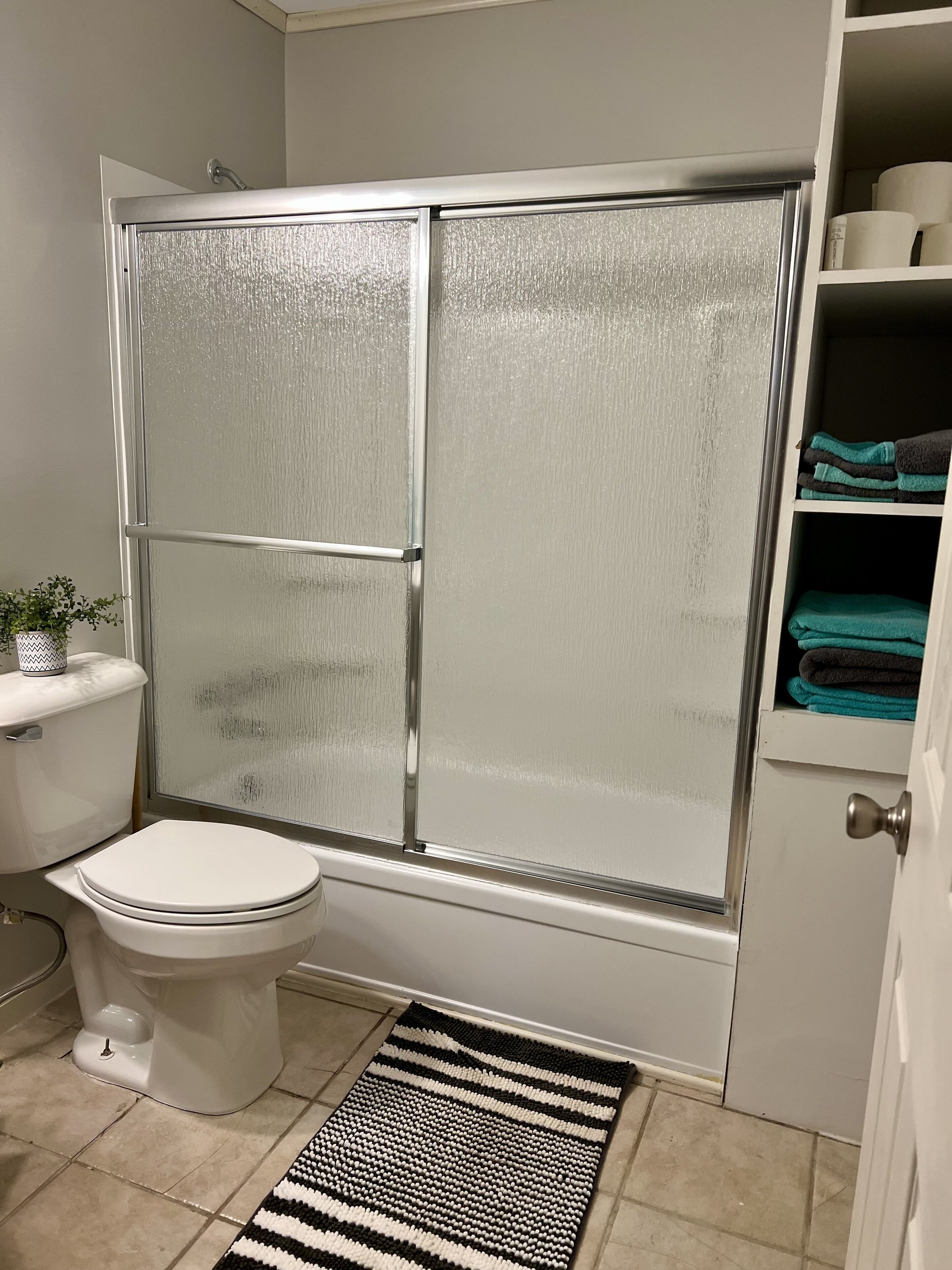 Un baño con cabina de ducha, inodoro y estante con toallas.