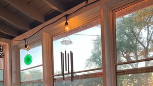 A cozy room with a wooden table and chairs, large windows with a view of a green landscape, and a hanging light fixture. - Screened porch, Lake Huron views, quiet sub, walk to beach and town in minutes! (Port Austin)