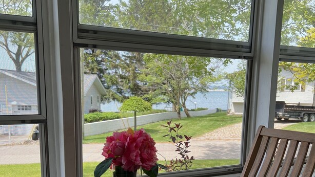 A wooden table and chairs by a window with a view of a house and trees. - Screened porch, Lake Huron views, quiet sub, walk to beach and town in minutes! (Port Austin)