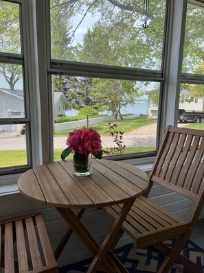 Een houten tafel en stoelen bij een raam met uitzicht op een huis en bomen.