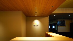 A reception desk with a wooden finish and a logo above it. - Hotel Sanraku (Yamanouchi)