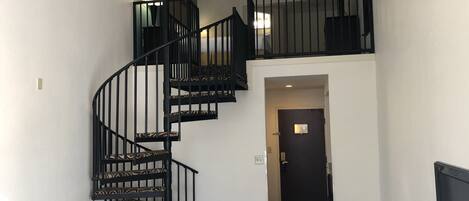 A spiral staircase with black railings and patterned carpet leading to a second-floor balcony.
