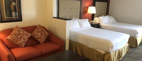 Una habitación de hotel con un sofá rojo, dos camas individuales, una mesita y un cuadro en la pared.