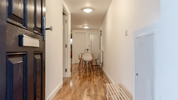 Een hal met houten vloer, een deur met een hendel, een witte muur en een plafond met inbouwspots.