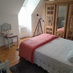 A bedroom with a bed, a chair, a telescope, and a wardrobe.