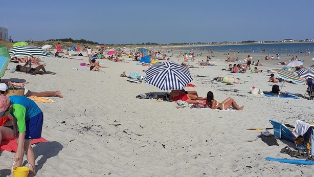 Une plage bondée, avec de nombreux parasols et des gens qui prennent des bains de soleil.