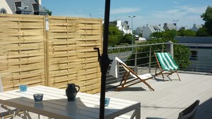 Une terrasse extérieure avec une table et des chaises en bois, un parasol violet et une chaise de plage à rayures vertes et blanches.