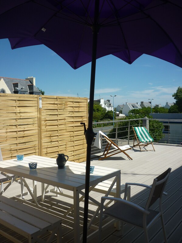 An outdoor patio with a wooden table and chairs, a purple umbrella, and a green and white striped beach chair.