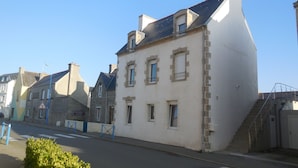 Une vue de rue d’un immeuble dont la façade est en pierre, avec de nombreuses fenêtres et un escalier apparent menant à un étage supérieur.