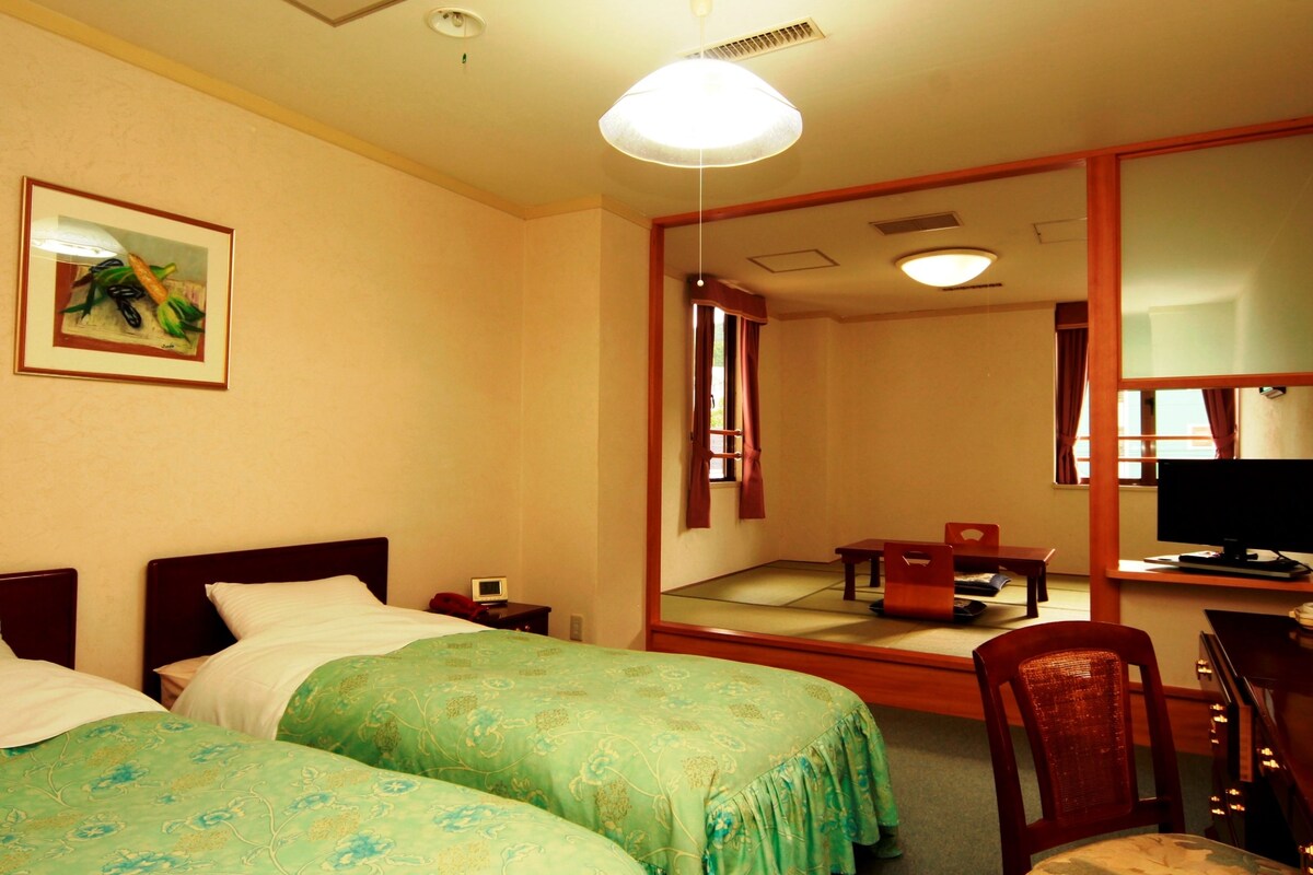 A hotel room with two beds, a desk with a computer, a chair, and a large mirror.