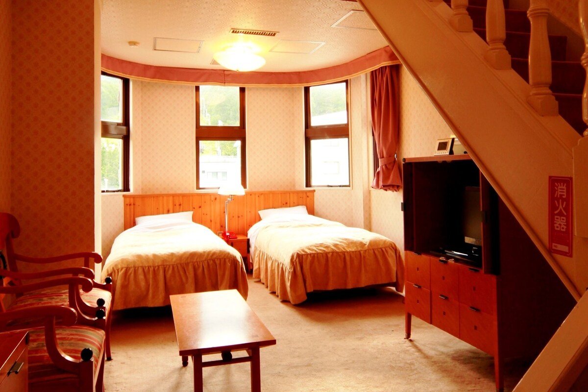 A bedroom with two beds, a wooden desk, a TV, and a staircase.