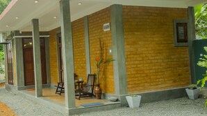 A covered outdoor area with a brick wall, concrete pillars, a wooden door, and a table with chairs. - Brown House (Unawatuna)