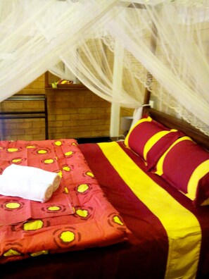 A bed with a red and yellow patterned bedspread, a white towel, and a striped pillow.