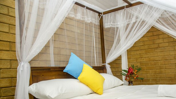 A bed with white bedding, a blue and yellow pillow, and a white canopy. - Brown House (Unawatuna)